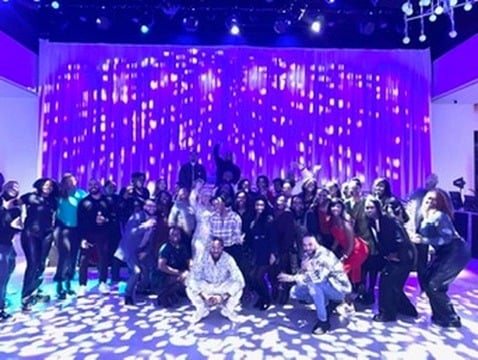 A large group of ADW Collective members photographed together under stage lighting.
